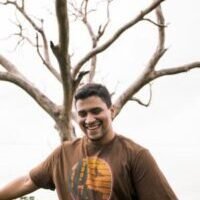 man in brown crew neck t-shirt standing beside bare tree during daytime