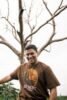 man in brown crew neck t-shirt standing beside bare tree during daytime